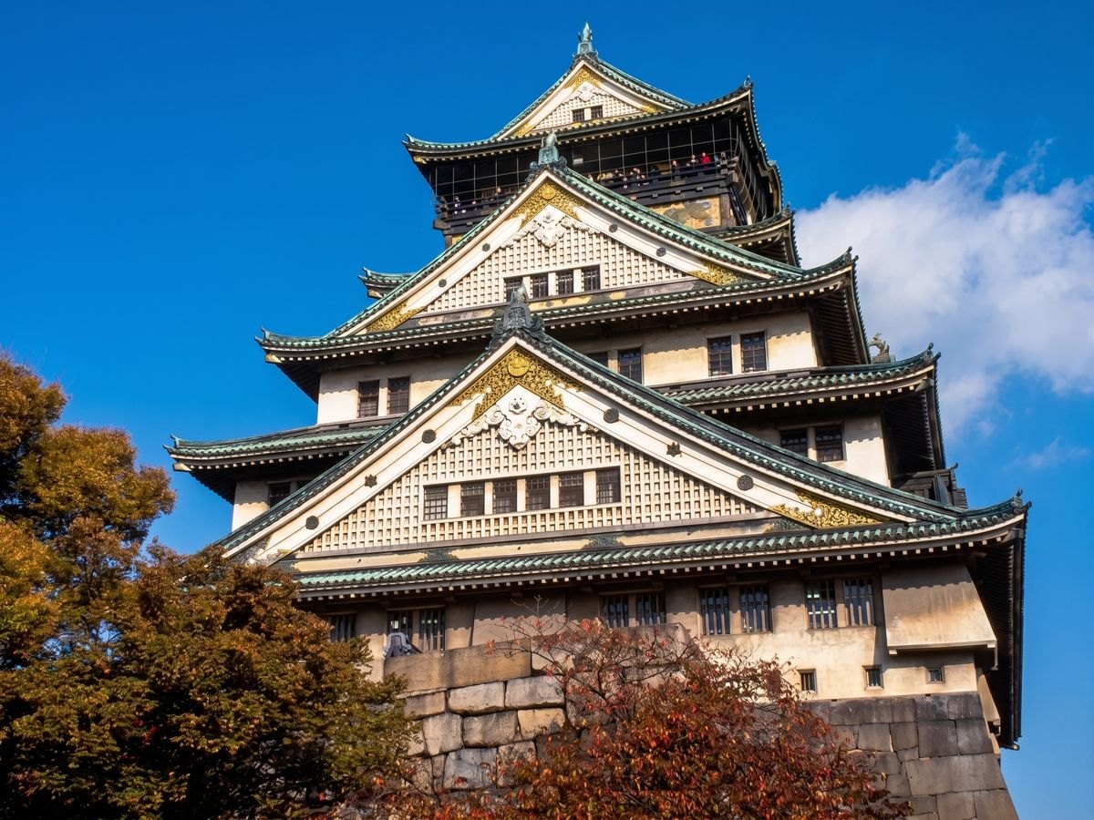 青空の下の大阪城天守閣と、秋の木々のイメージ写真