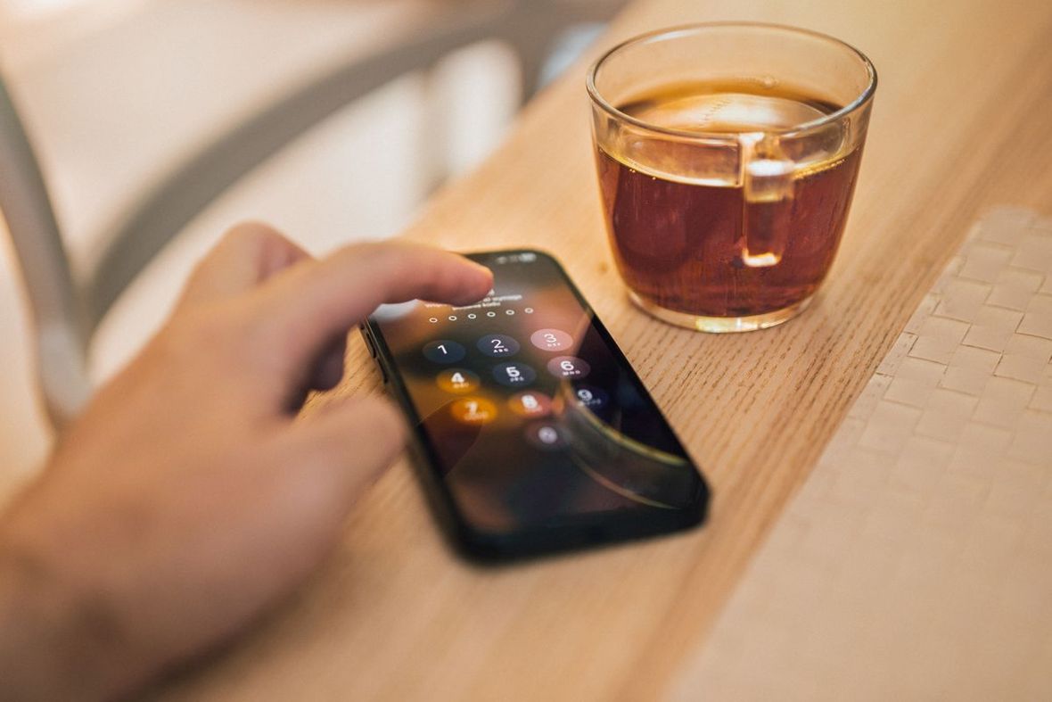 テーブルの上のスマホの画面ロックを、指で操作しているイメージ写真